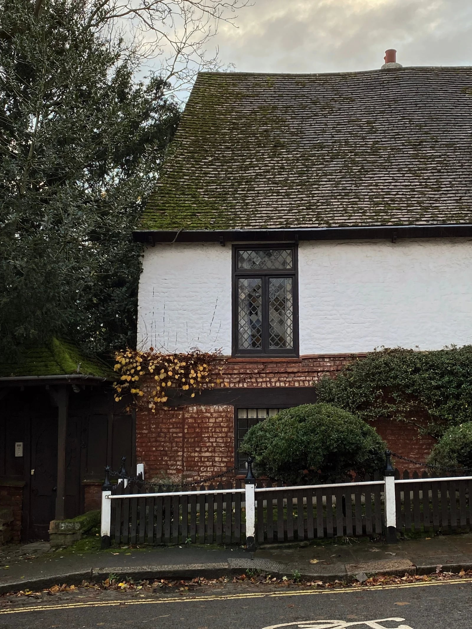 A traditional cottage with an aged tiled roof, white walls and clipped hedges in Greater London