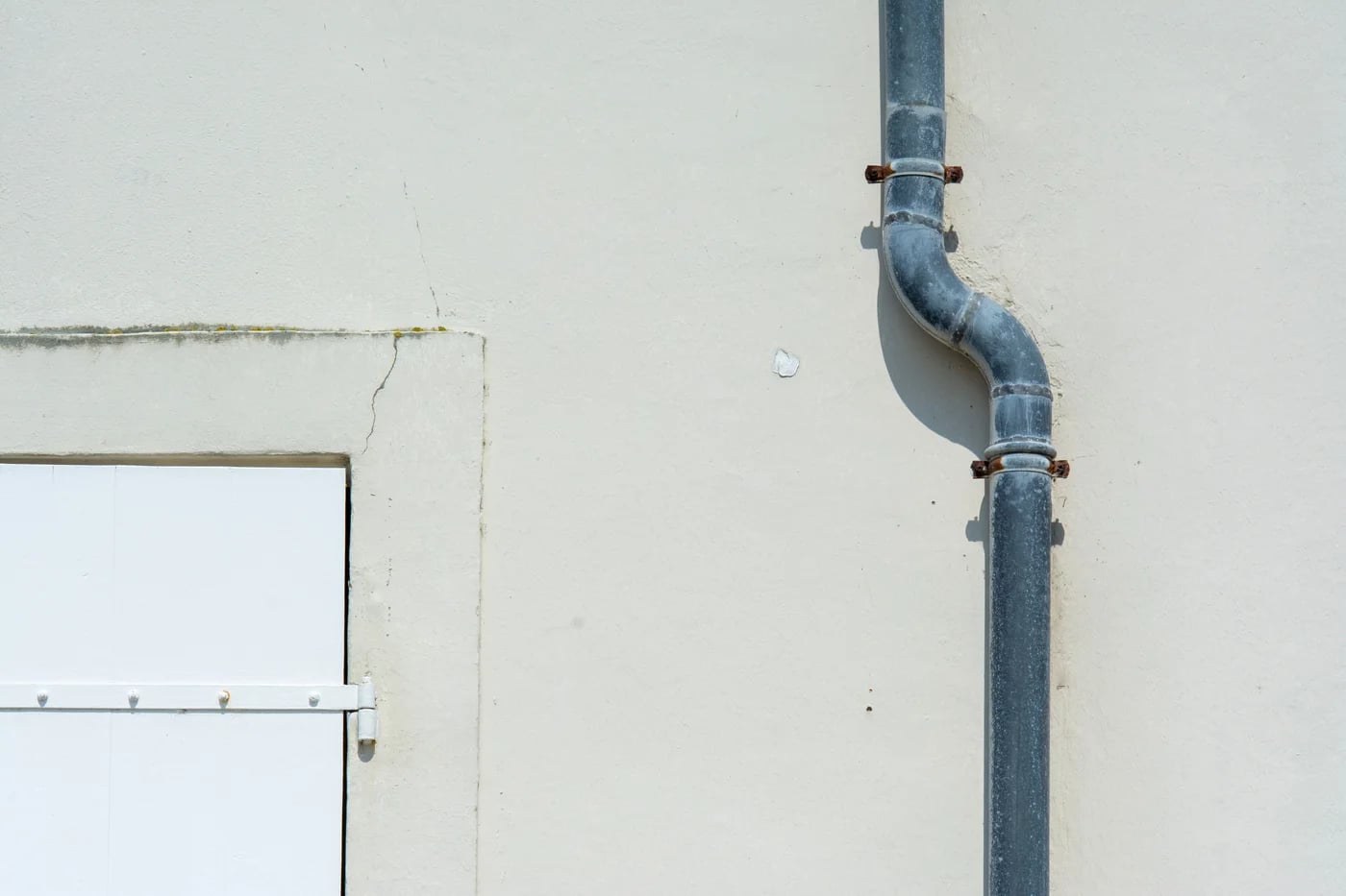 Grey metal rainwater downpipe against a pale rendered wall